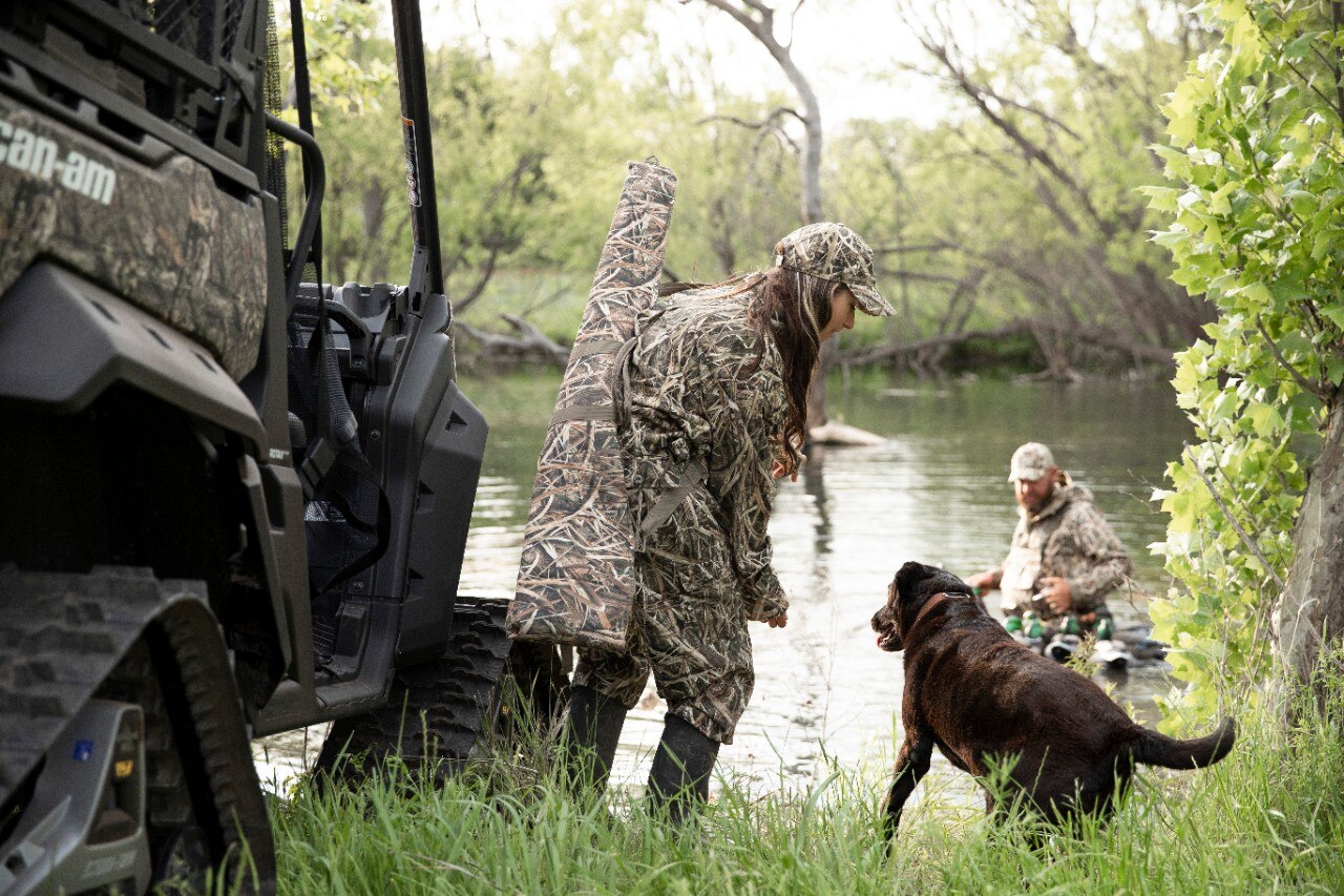 A girl and his god hunting beside a customized Can-Am Defender Mossy Oak Edition side-by-side