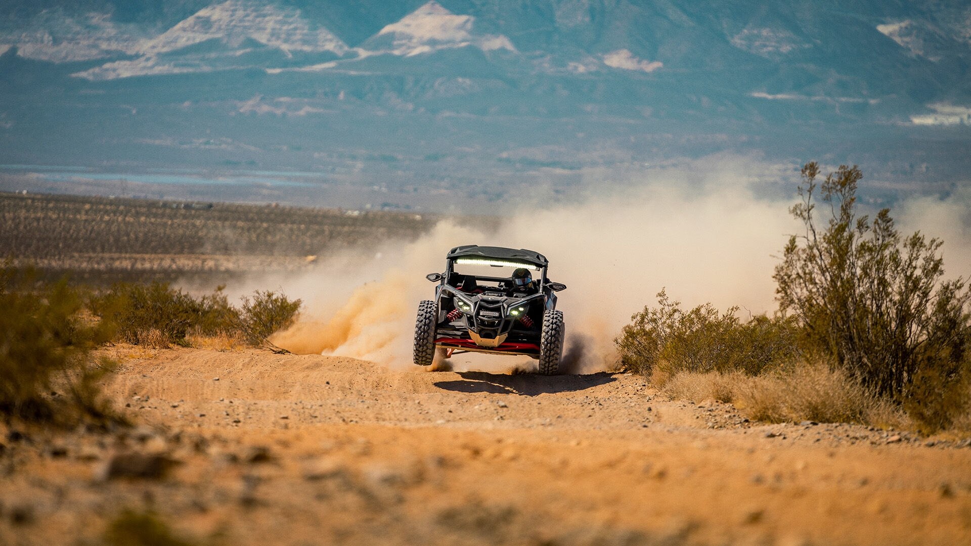 A Can-Am side-by-side racing across the desert rocks, leaving a trail of dust in its wake