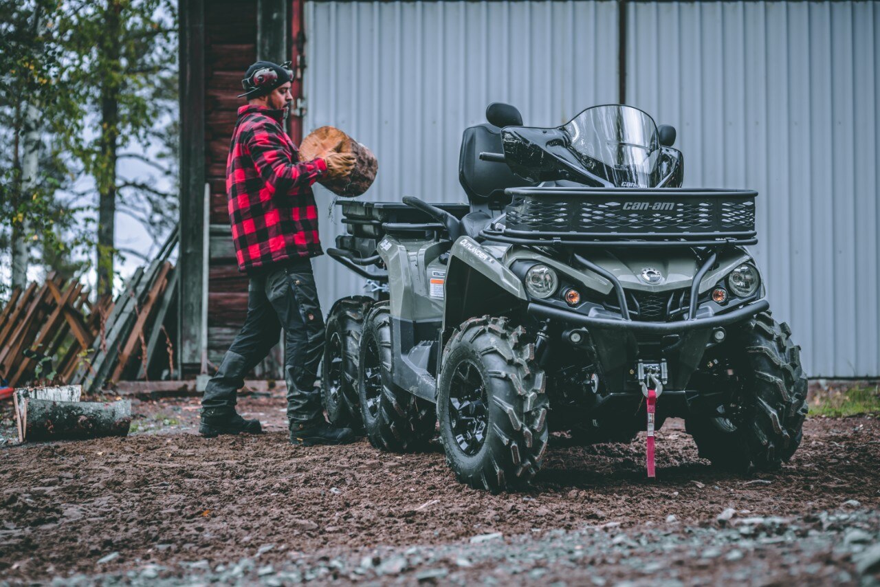 Un hombre poniendo madera en una canasta en la parte trasera de su ATV Can-Am Outlander de 2 asientos