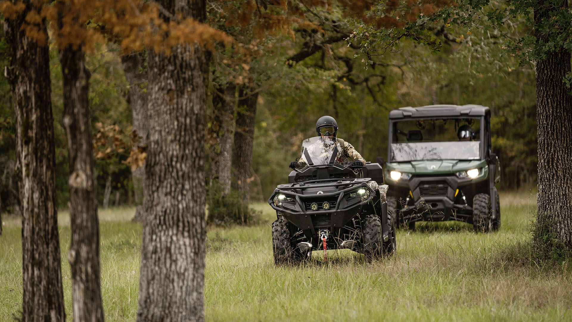 Un Can-Am Defender side-by-side y un Outlander ATV siguiéndose el uno al otro por el bosque, listos para ir de caza