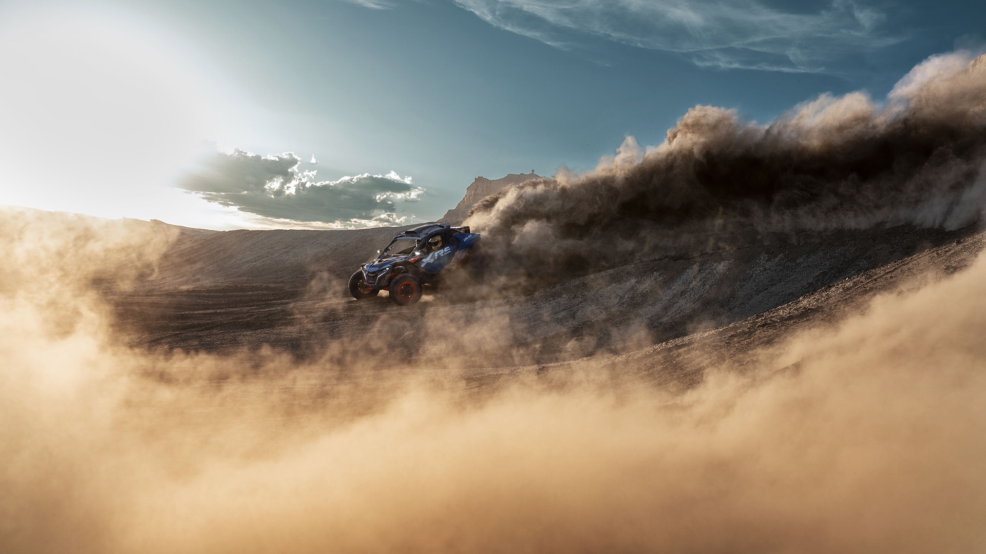 A Can-Am Maverick R X RS SAS driving through the desert, leaving a huge trail of dust behind it.