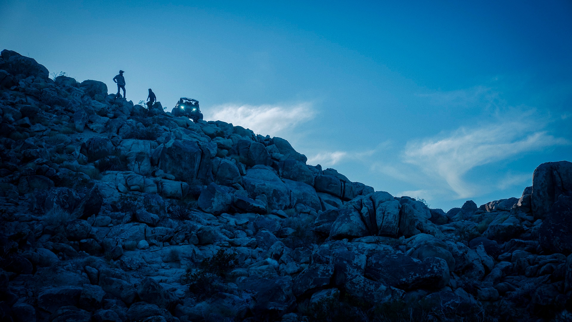 Una montaña de roca con dos pilotos y un 2026 Can-Am Maverick R X RC en la cima