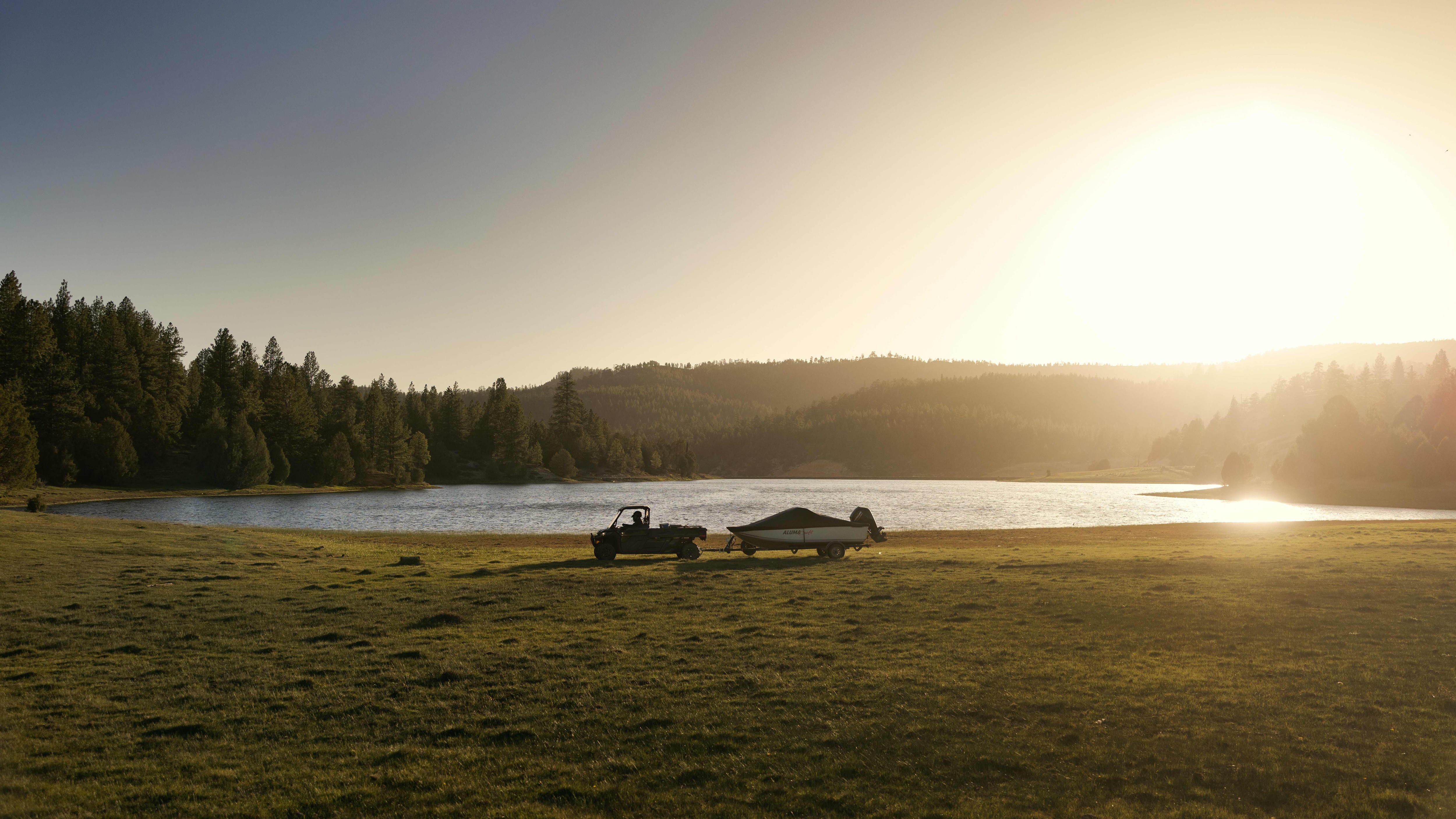A Can-Am side-by-side towing a boat near a lake at sunset