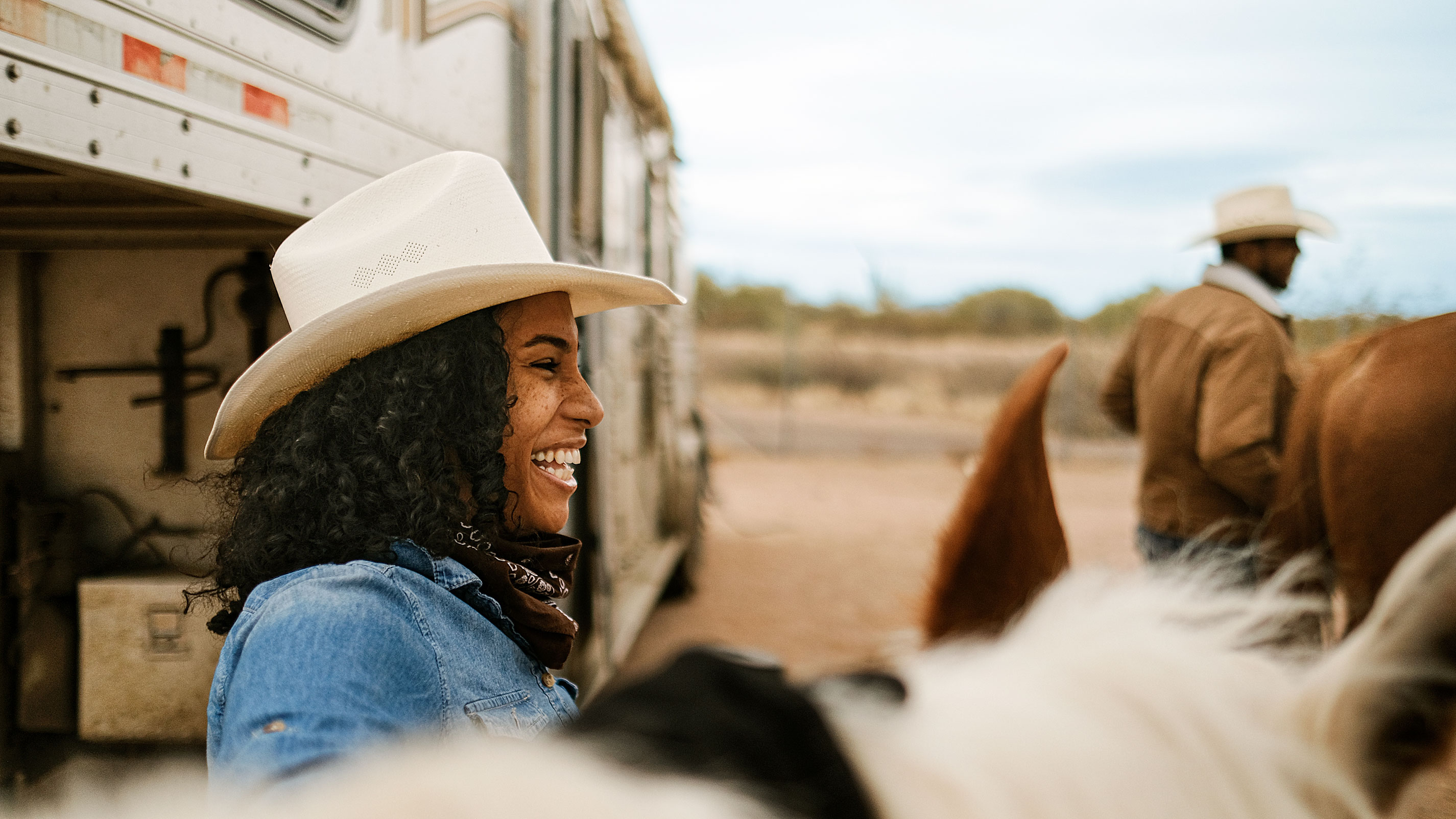 Uma vaqueira sorrindo ao lado de cavalos