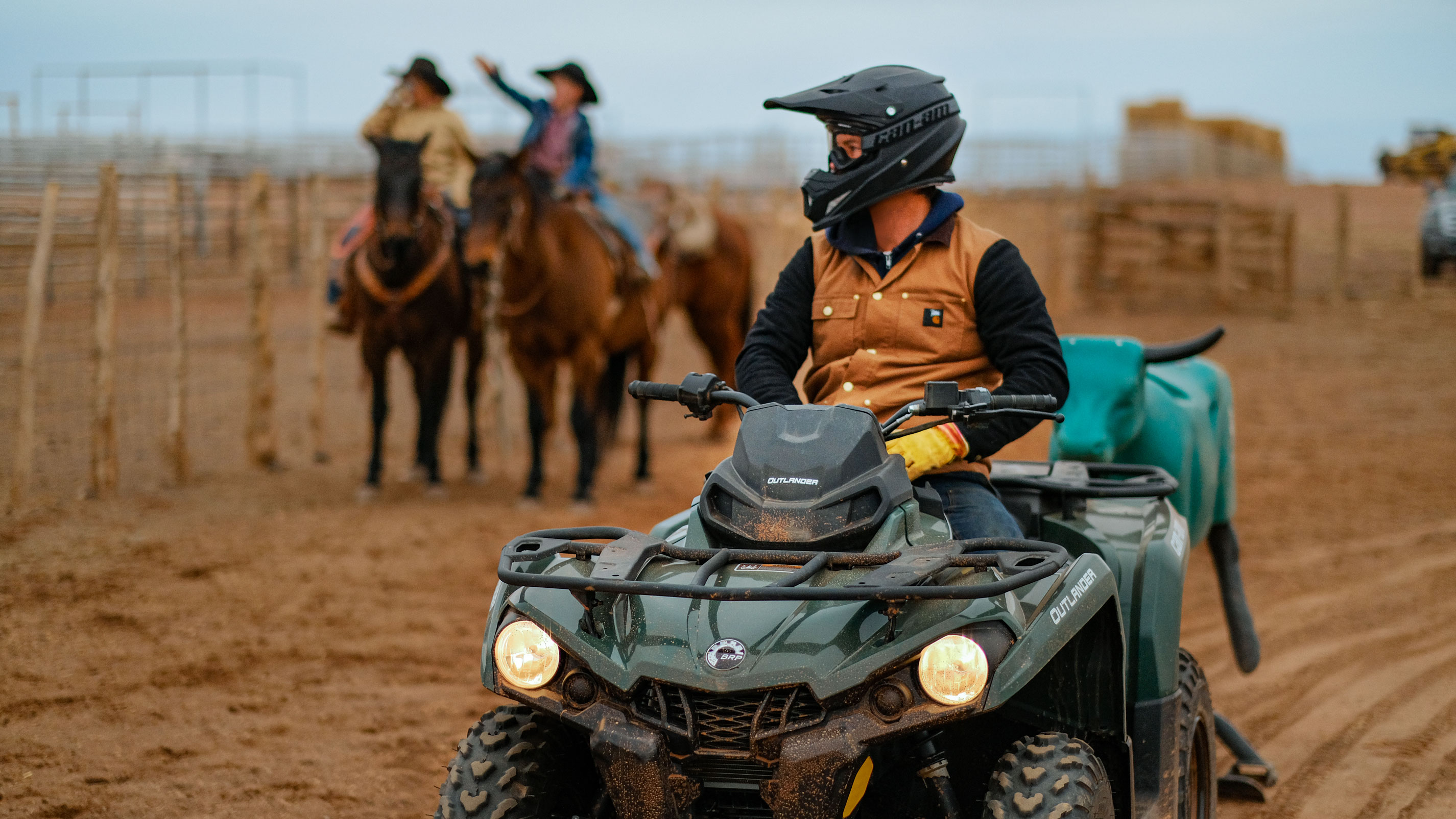 Um homem em um quadriciclo perto de vaqueiros em um rancho