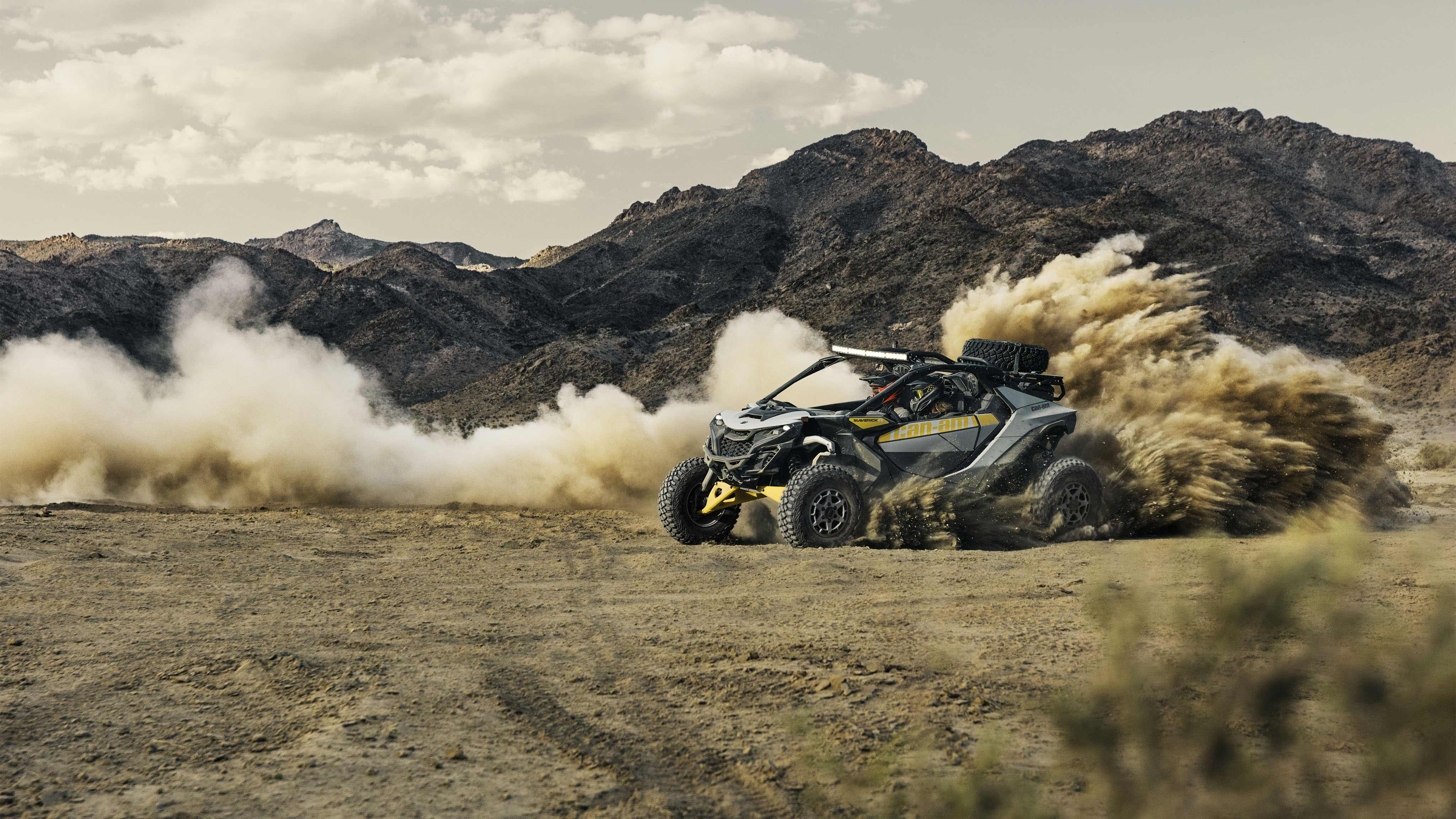 Two riders in a Can-Am Maverick R SxS vehicle speeding through the desert